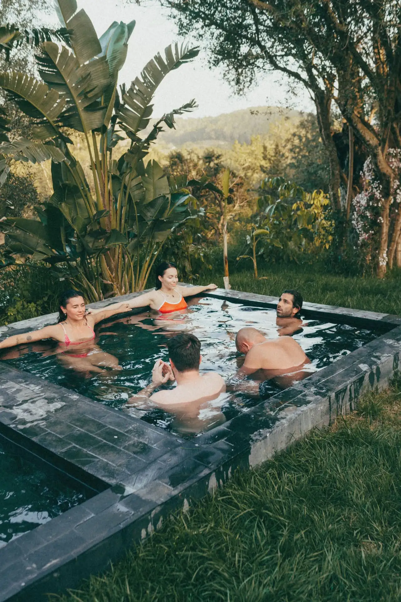 Guests sitting together in a stone plunge pool surrounded by garden at golden hour
