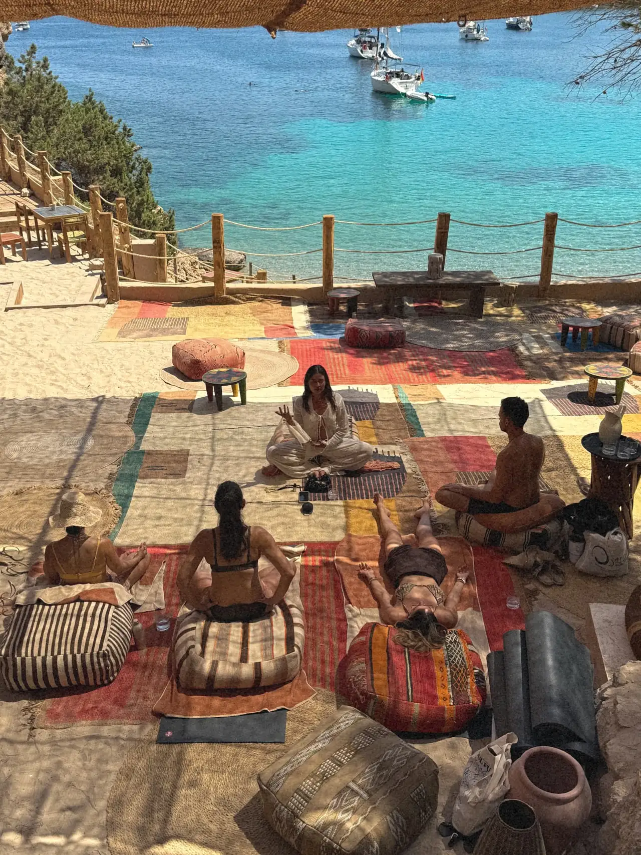 A seated circle on rugs above a turquoise cove