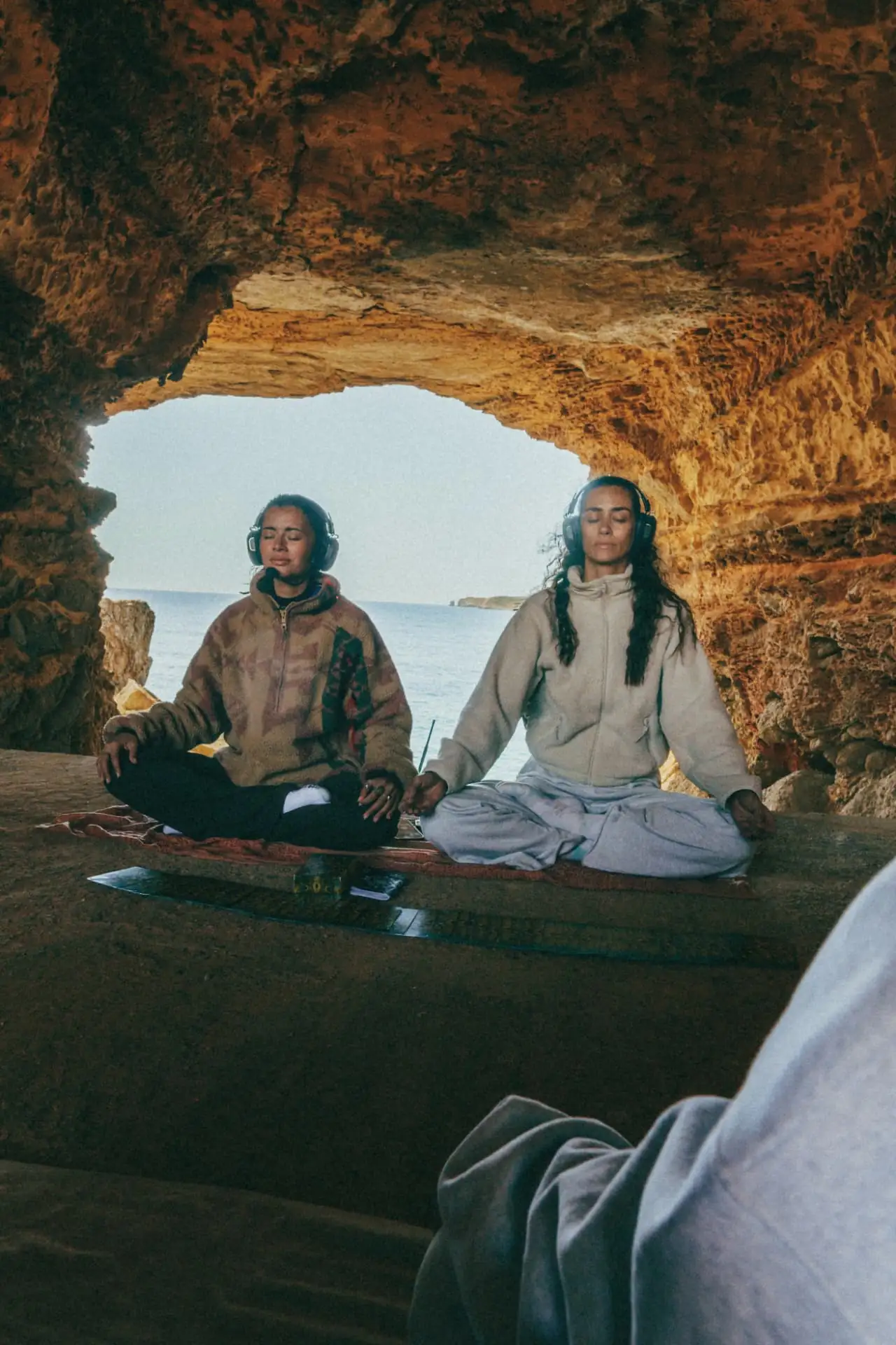 Two women meditating in a sea cave above the water at sunrise